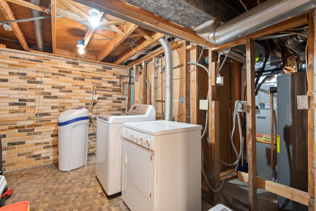 A basement laundry room with a water heater beside the appliances