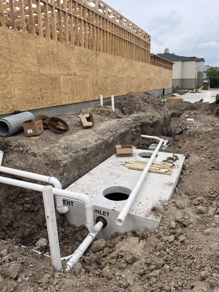 A concrete grease trap set in an open trench with the inlet and outlet piped