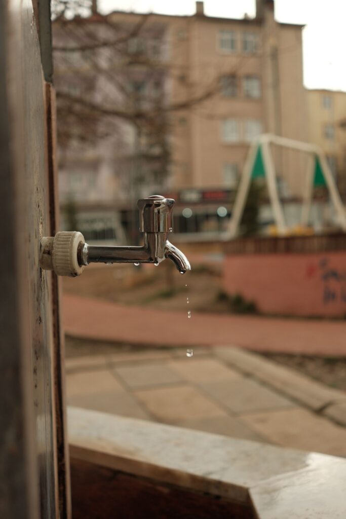 An outdoor tap dripping at the wall of a building