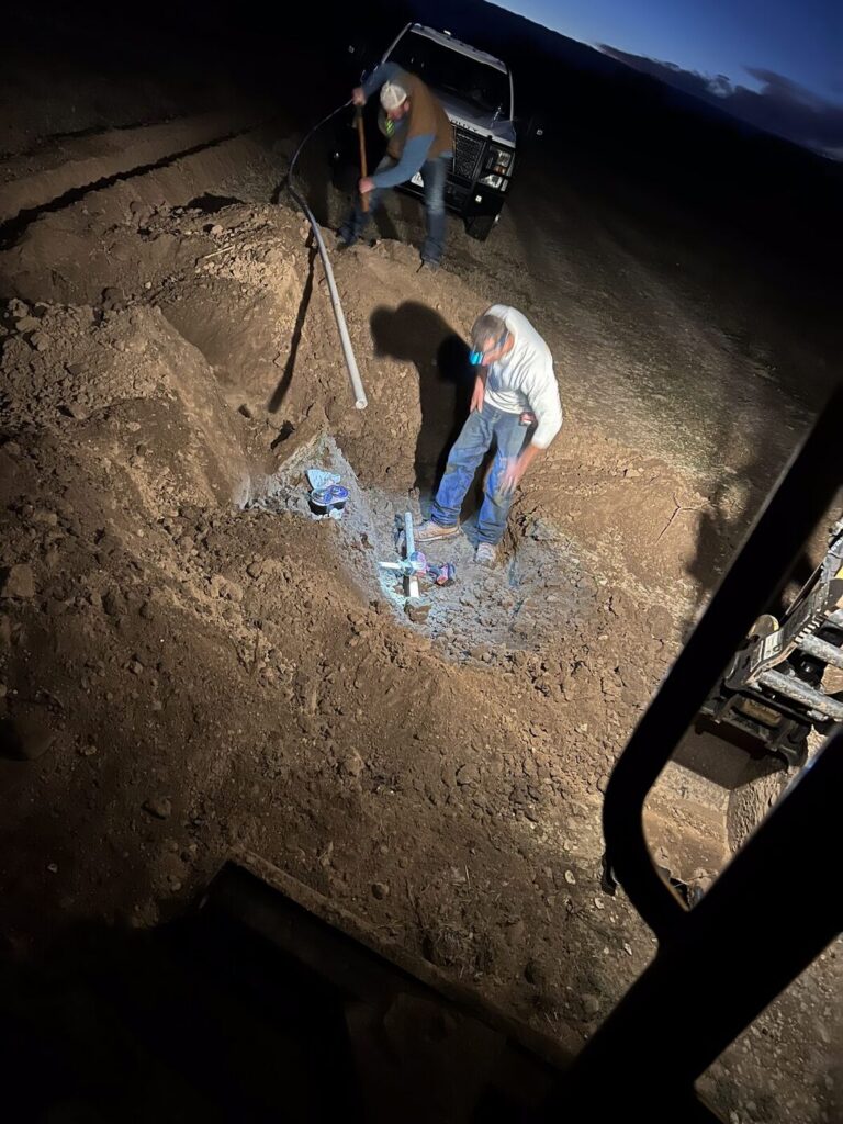 An open trench lit at night during a water line repair