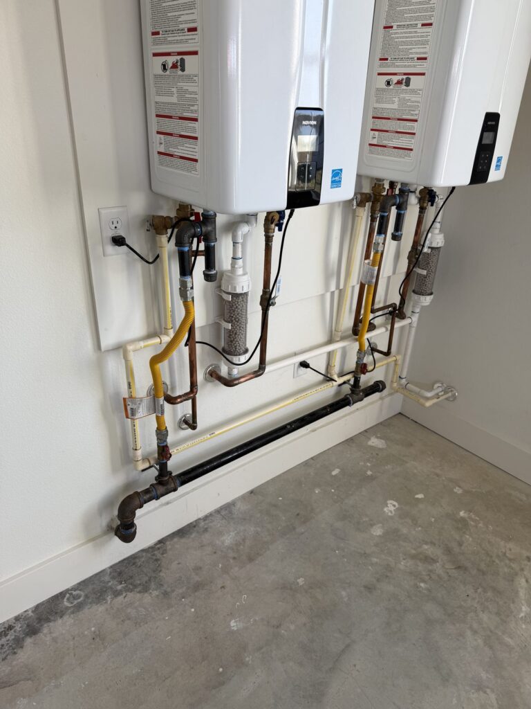 Two tankless water heaters installed side by side with gas and water connections