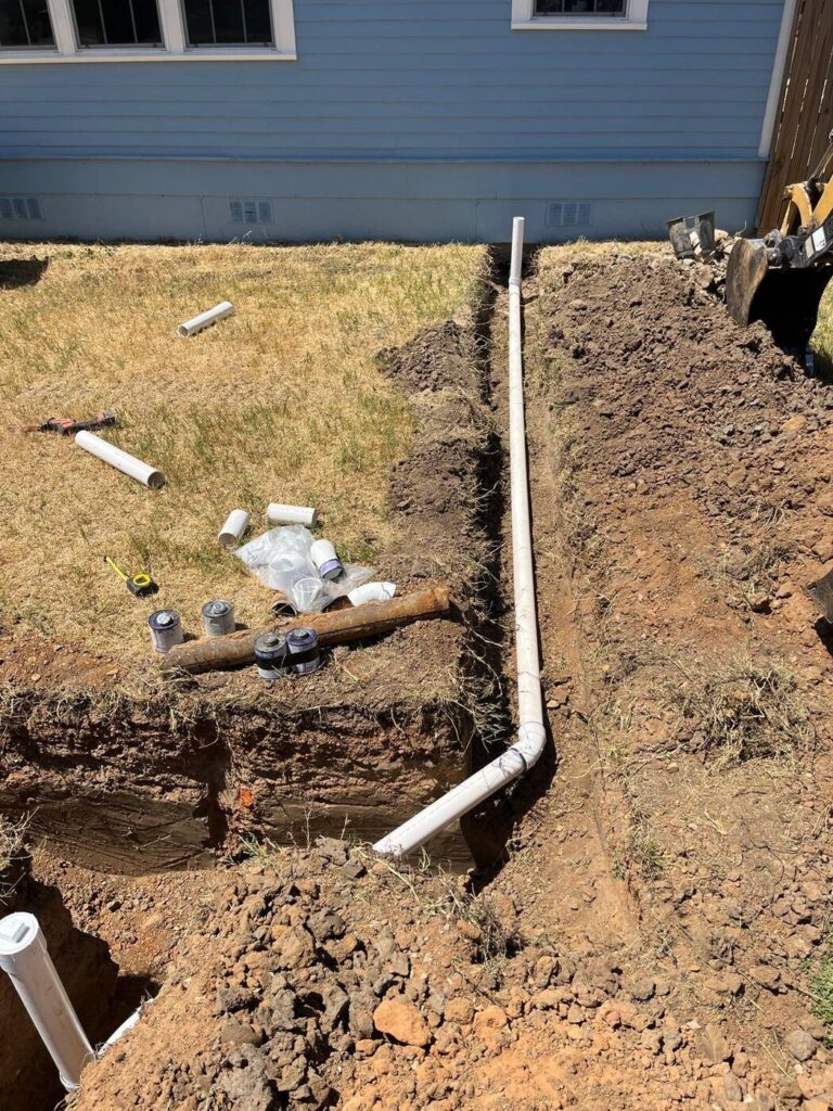 A new sewer yard line laid in an open trench beside a house