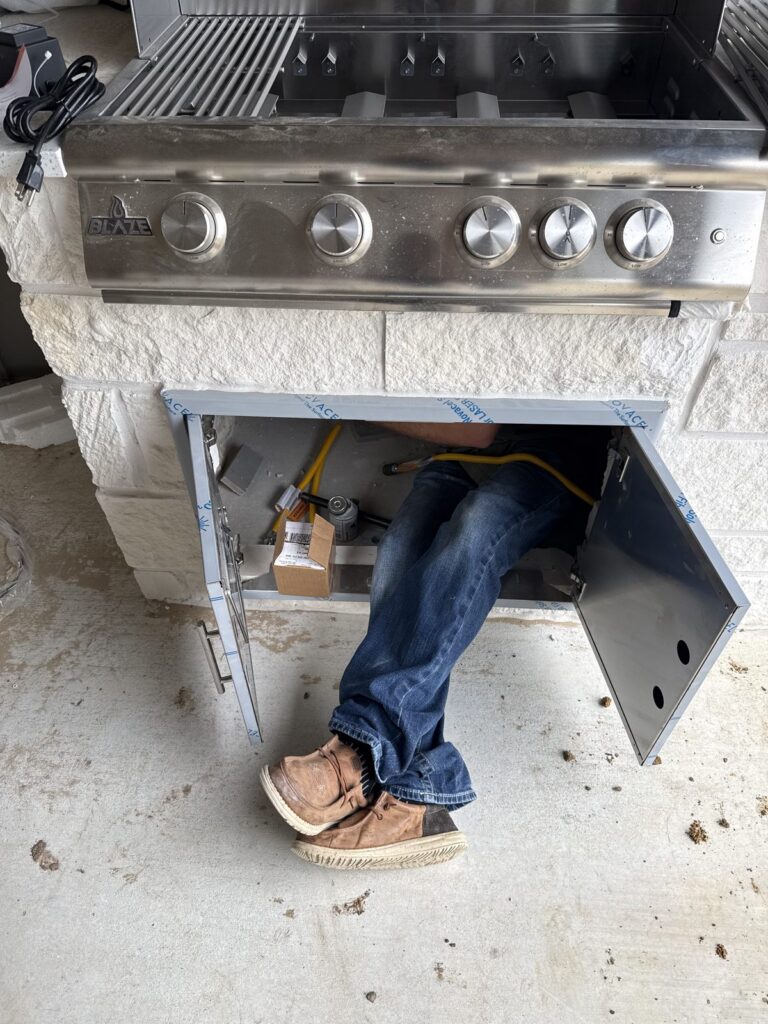 A plumber working inside the cabinet of an outdoor kitchen grill