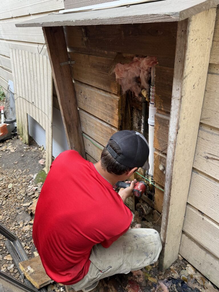 A plumber working on supply piping inside an outdoor utility closet