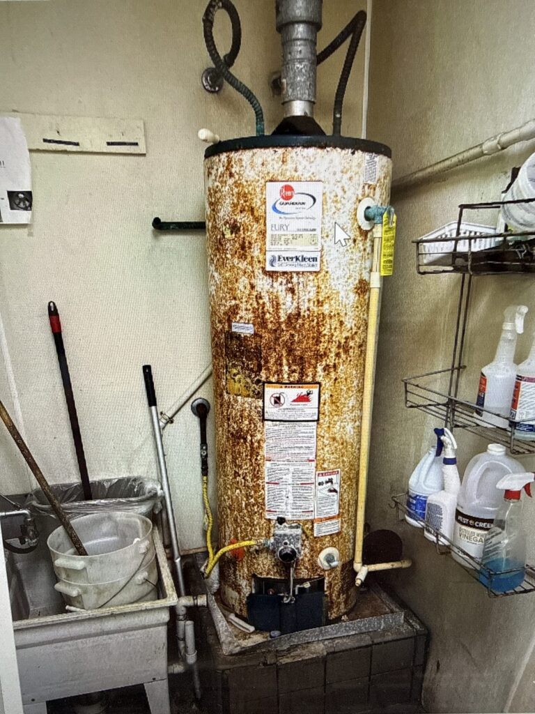 A badly rusted water heater in a utility room waiting to be replaced